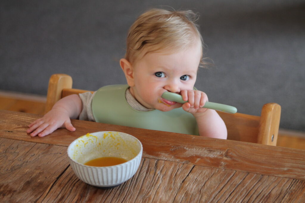 baby eating baby food out of bowl at wooden table