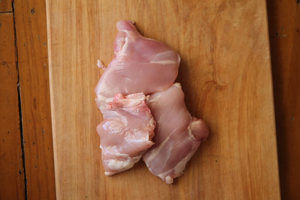 Raw chicken thighs on wooden chopping board