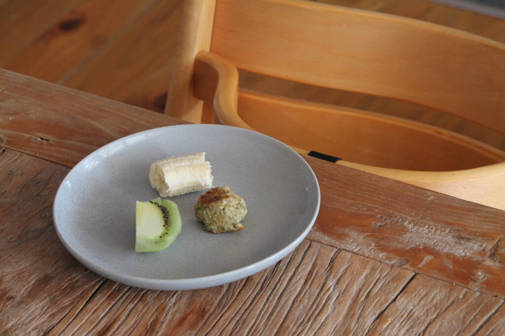 plate on table with chicken meatball banana and kiwifruit in front of high chair