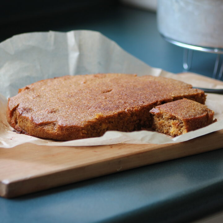 whole orange cake cut into with one piece exposed on wooden cutting board