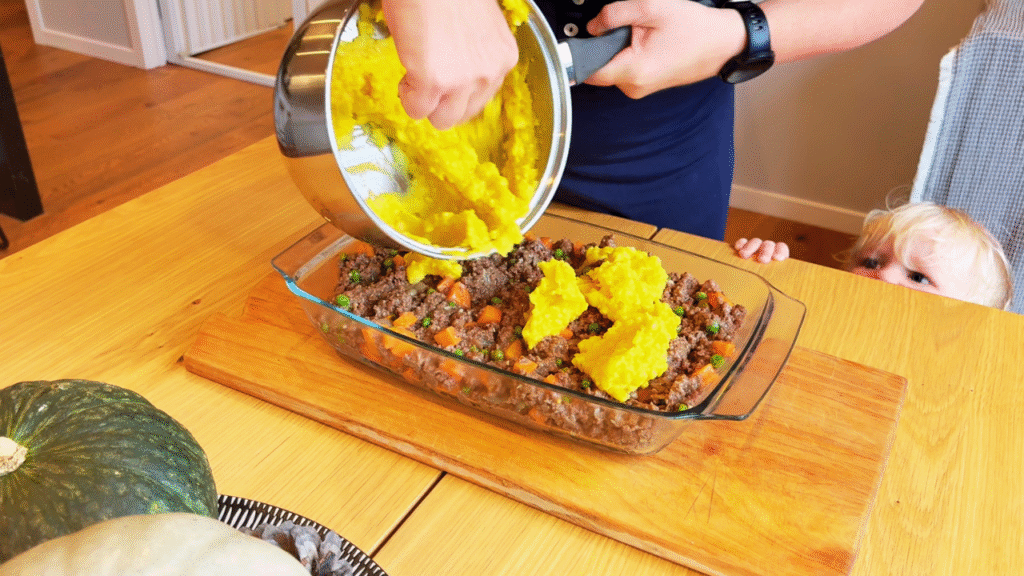 Toddler helping to meal prep cottage pie on a wooden table