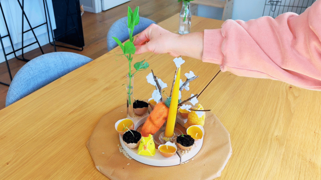 A plant being placed on spring center piece on wooden table for spring rhythm with toddlers