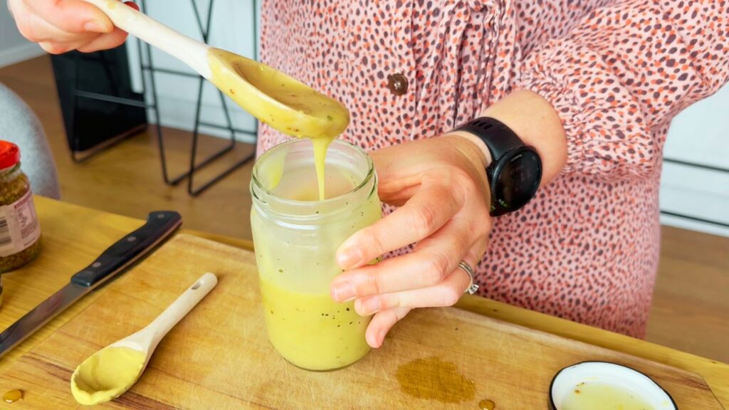 honey mustard dressing dripping off wooden spoon into glass jar