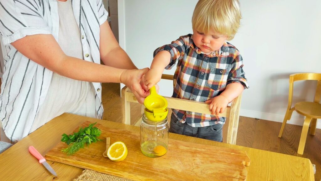 toddler helping to squeeze lemon juice to make seed oil free herb mayo