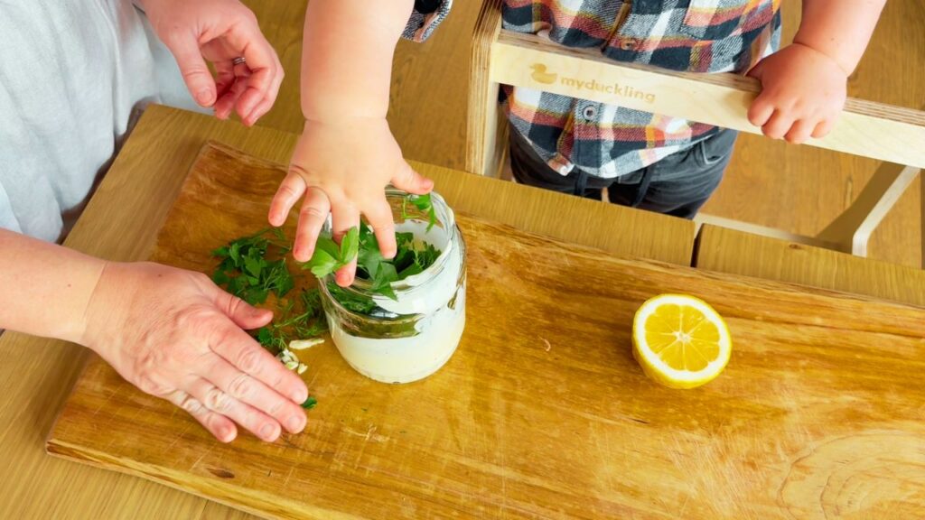 toddler helping to add parlsey and dill to make seed oil free herb mayo
