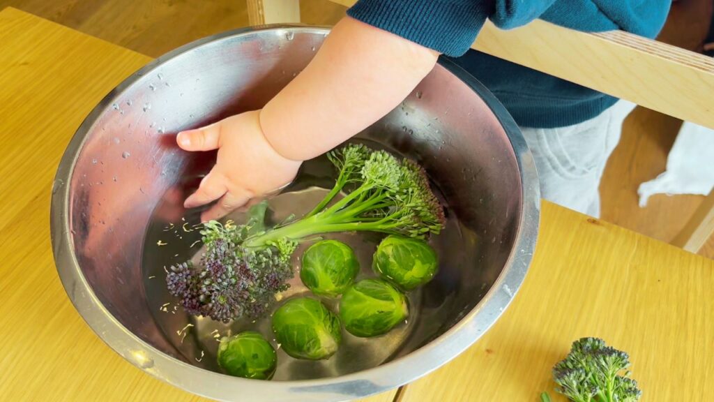 toddler helping to wash broccoli and brussel sprouts