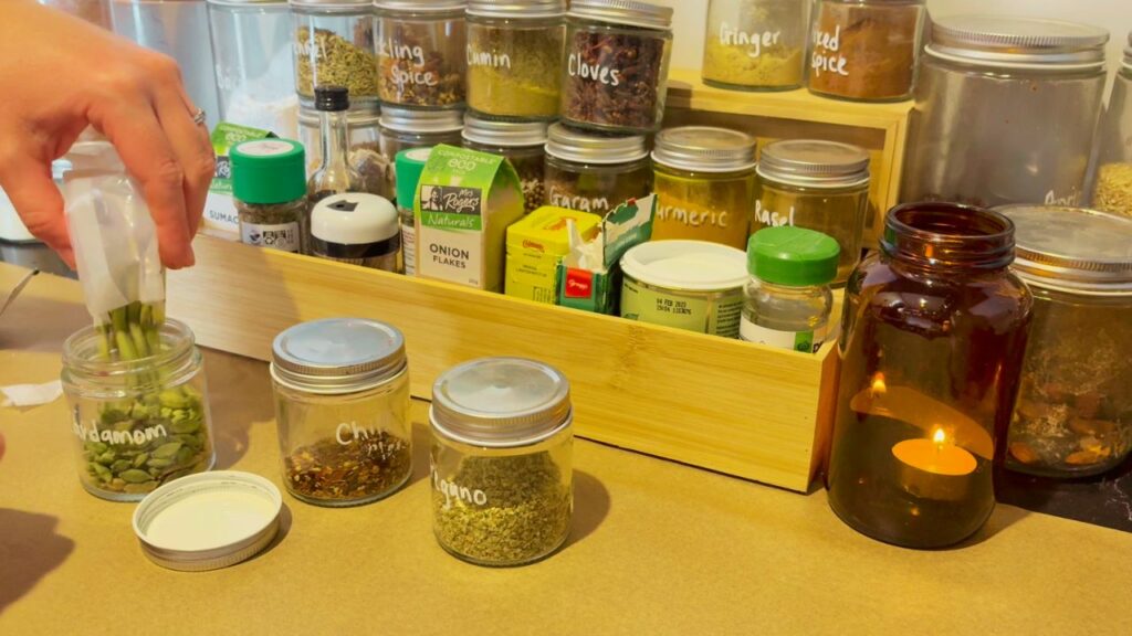 Organized spice and pantry jars labeled with ingredients like cumin, cocoa powder, and fennel — part of a kitchen refresh for a new year of flow