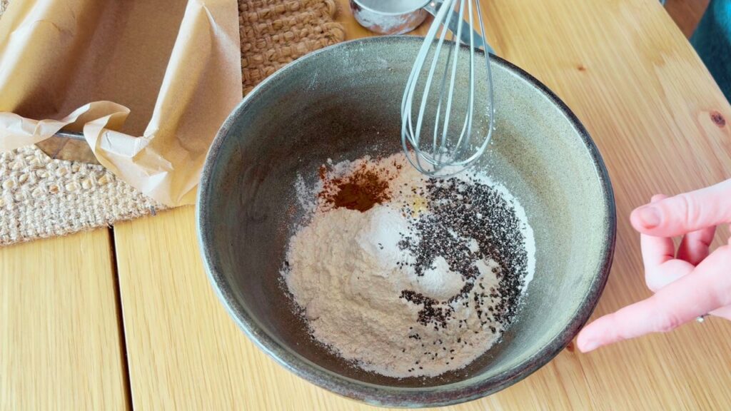 Mixing spelt flour, cinnamon, chia seeds, and baking powder in a ceramic bowl to prepare the dry ingredients for gut friendly carrot cake.