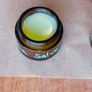 Two amber jars of finished plantain salve cooling on parchment paper after pouring.