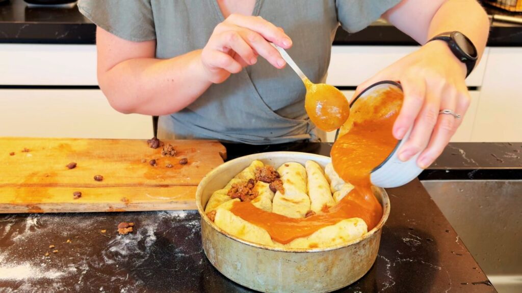 A woman pours rich tomato sauce over rolled enchiladas in a round baking dish, showing real-food holiday cooking made simple.