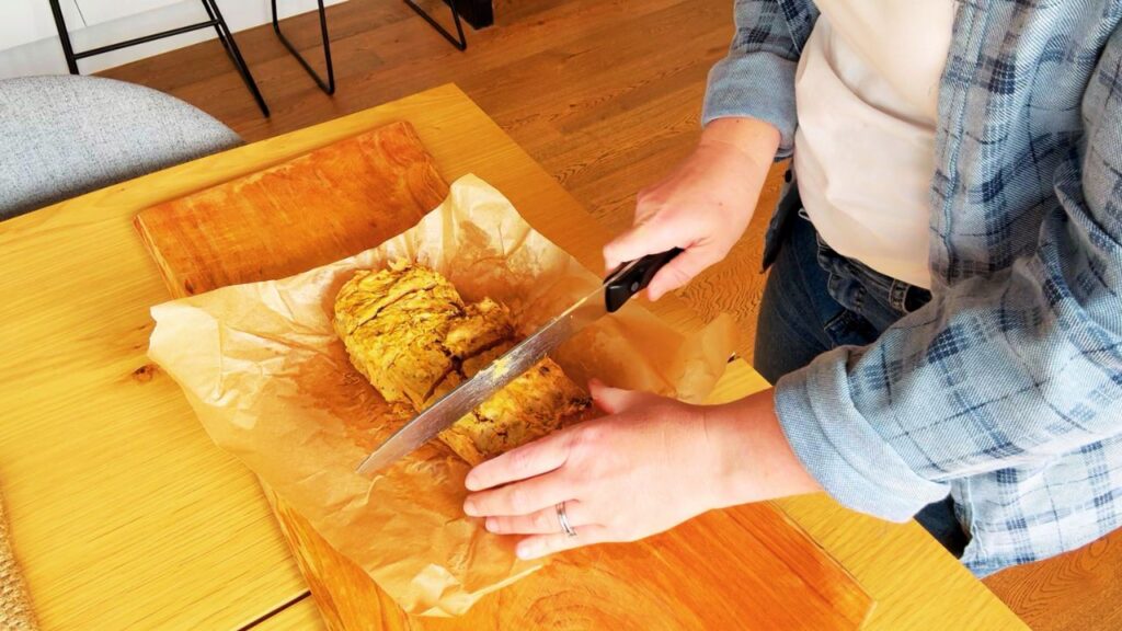 Cutting freshly baked gut friendly carrot cake into slices on a wooden board lined with parchment paper.