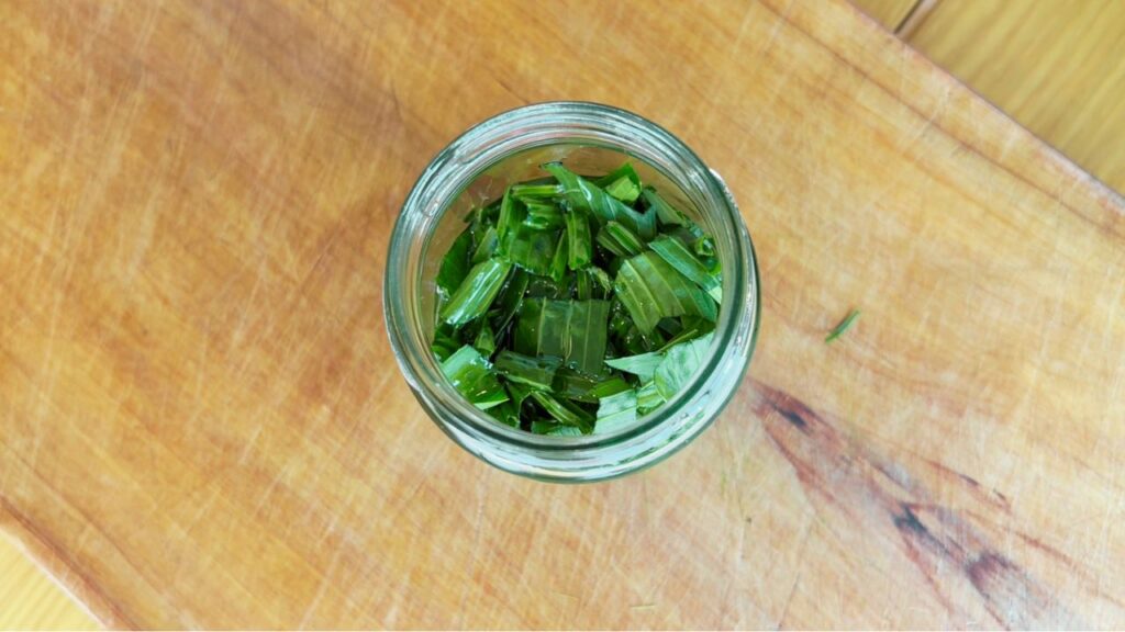 Top view of chopped plantain leaves soaking in coconut oil for a gentle family skin balm.