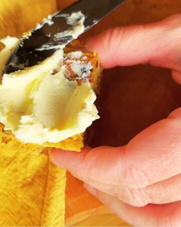 Spreading cream cheese frosting onto a slice of gut friendly carrot cake with a butter knife, held in hand over a yellow napkin.