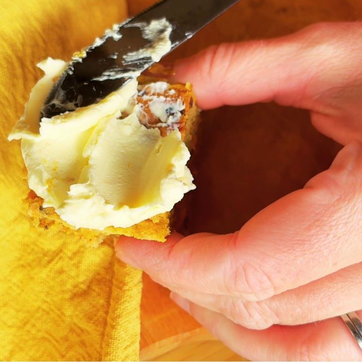 Spreading cream cheese frosting onto a slice of gut friendly carrot cake with a butter knife, held in hand over a yellow napkin.