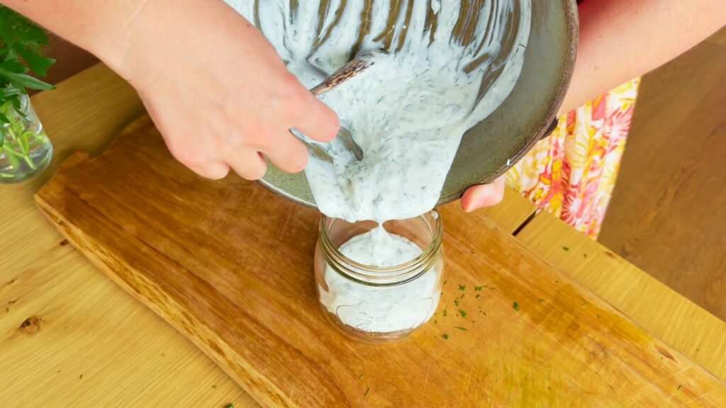 Pouring creamy homemade ranch dressing into a glass jar, highlighting its fresh herbs and probiotic-rich texture — part of a gut-microbiome-supportive kitchen.