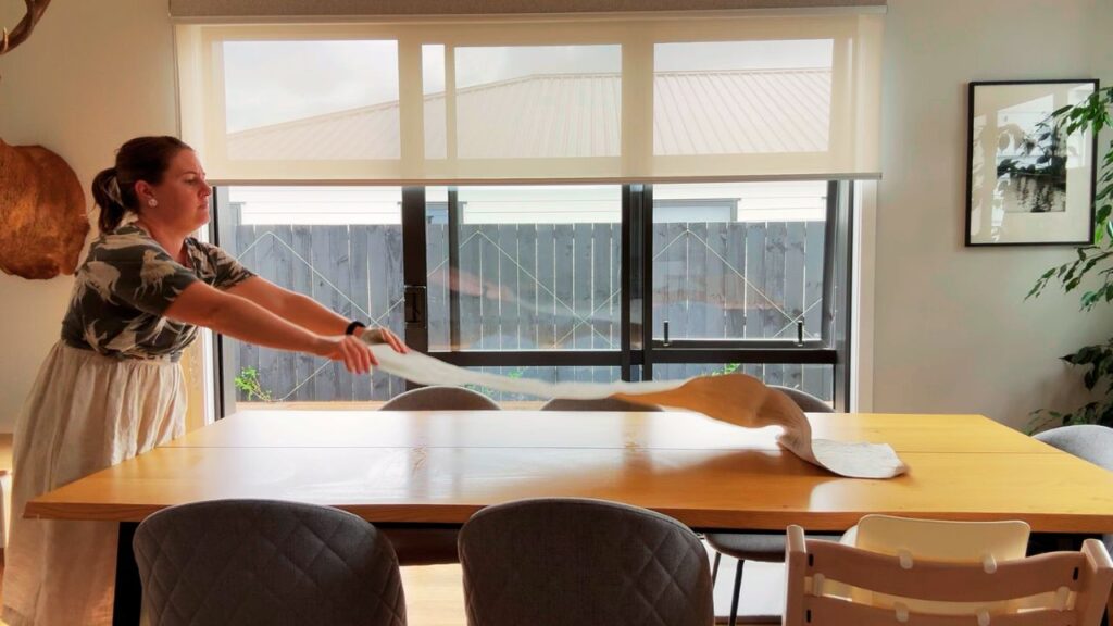A woman spreads a linen table runner across a wooden dining table, setting the tone for calm, nourishing holiday meals at home.