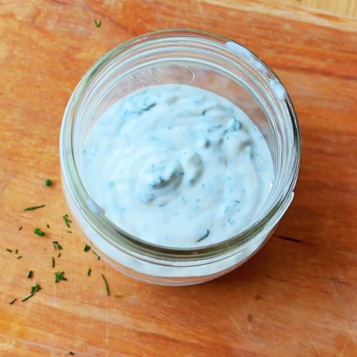 A jar of creamy probiotic ranch dressing on a wooden board, speckled with herbs — a simple, seed-oil-free recipe that supports gut health and real-food living.