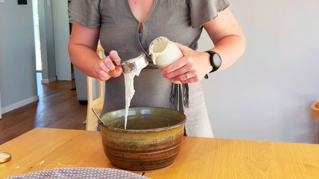 Adding flour and starter to a mixing bowl while making healthy seed-oil-free sourdough bread at home.