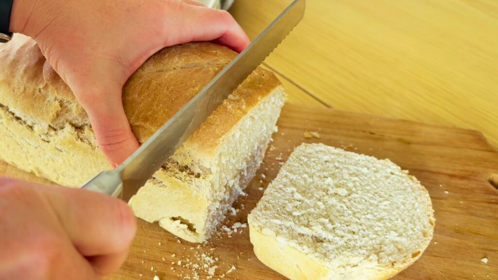 Cutting into a freshly baked sourdough sandwich loaf made without seed oils or vegetable oil.