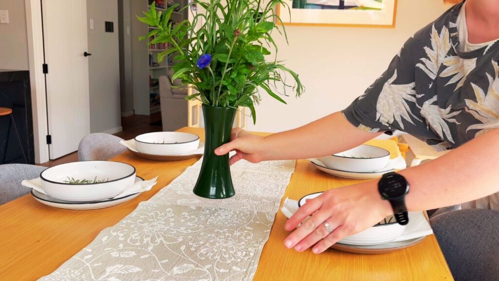 A calm, sunlit dining table set with simple white bowls, linen napkins, and a vase of fresh herbs and flowers — creating a peaceful, nourishing holiday table setting.