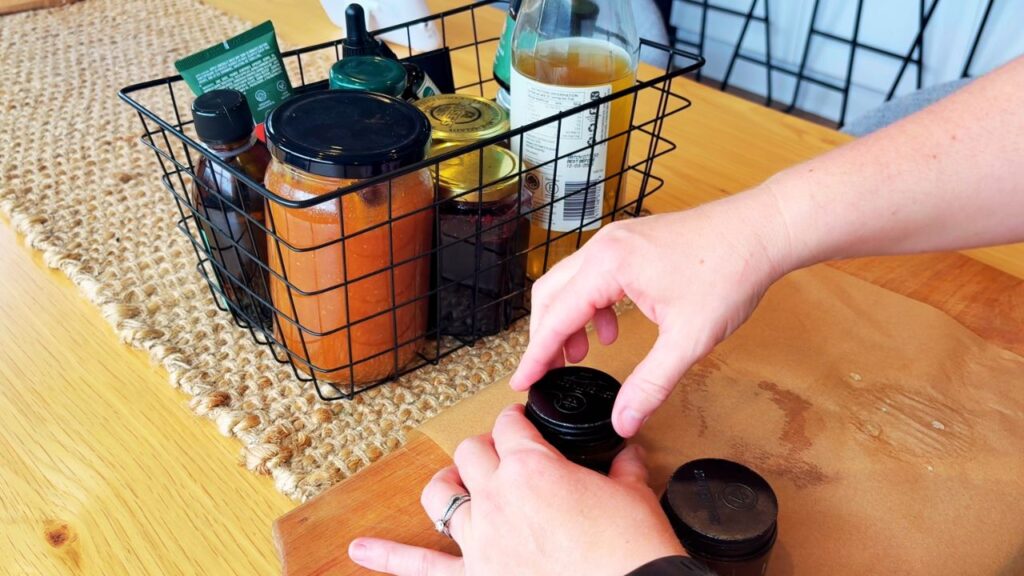 Packing jars of homemade plantain salve into a small household remedy basket with honey and herbal tonics.