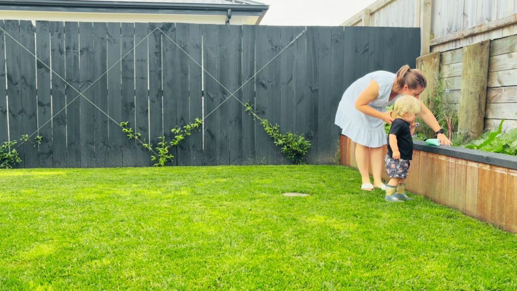 Mother and toddler exploring the backyard garden, checking plants and seedlings together