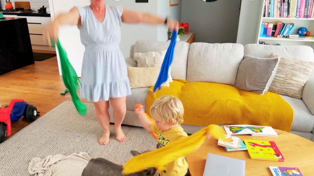 Mother and toddler joyfully dancing with colorful play silks in the living room.