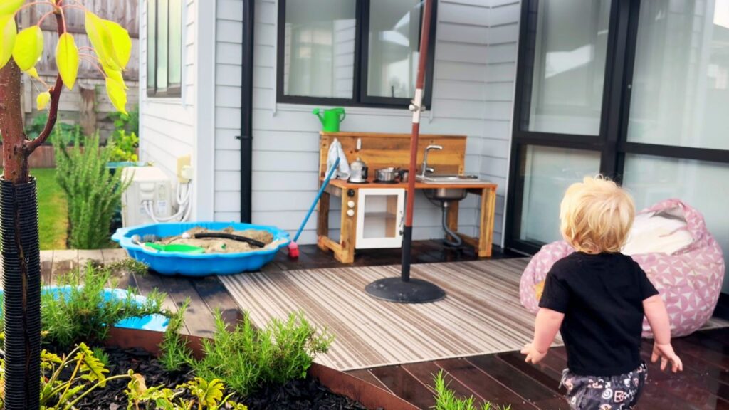 Toddler heading toward a wooden outdoor mud kitchen setup for simple backyard play.