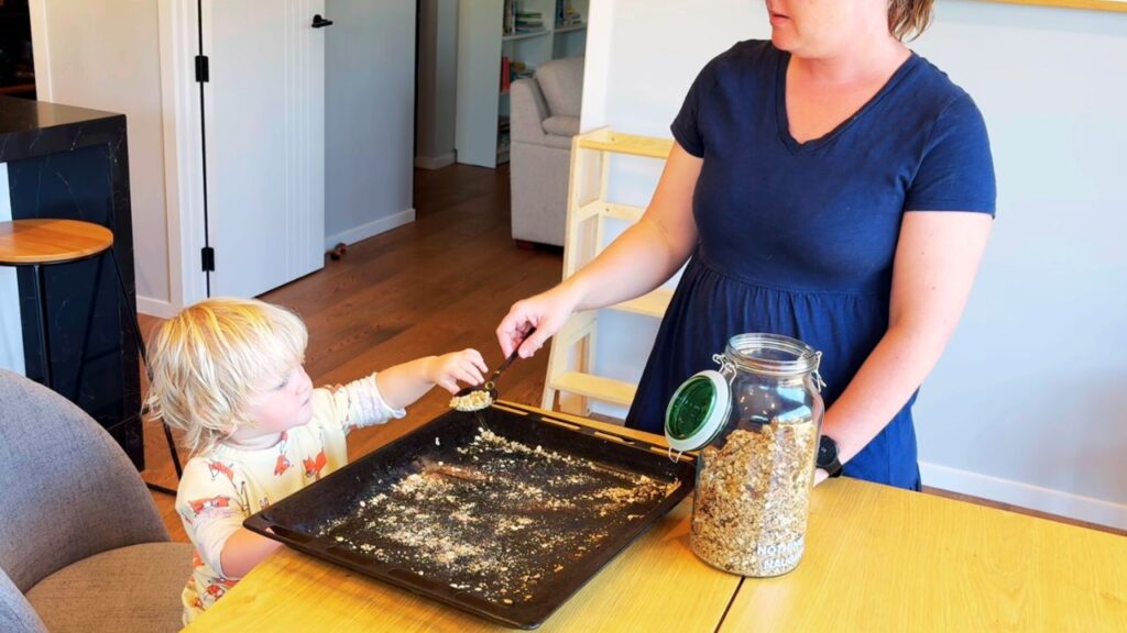 Mother and toddler making homemade granola together at the table, with jarred granola ready for breakfast