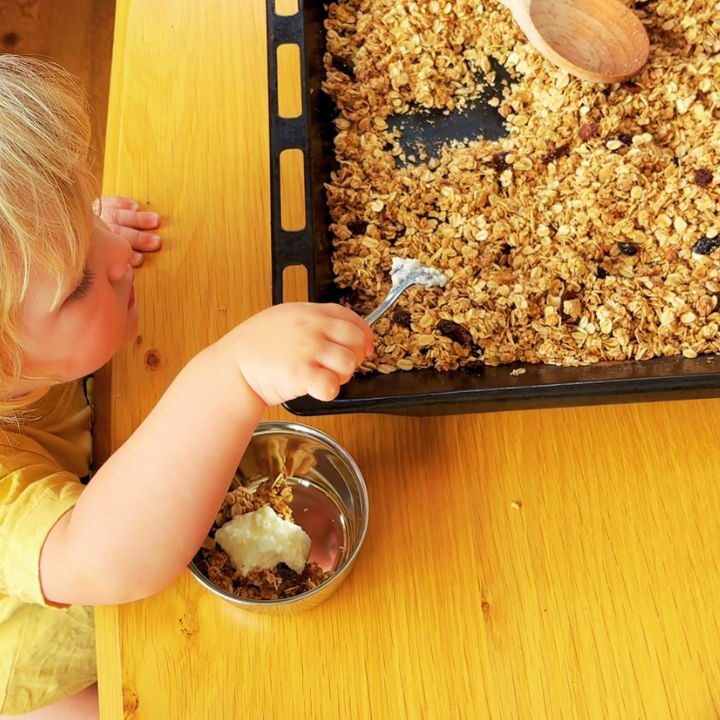Toddler serving himself homemade granola with yoghurt at the table, part of our simple gut-friendly breakfast rhythm.