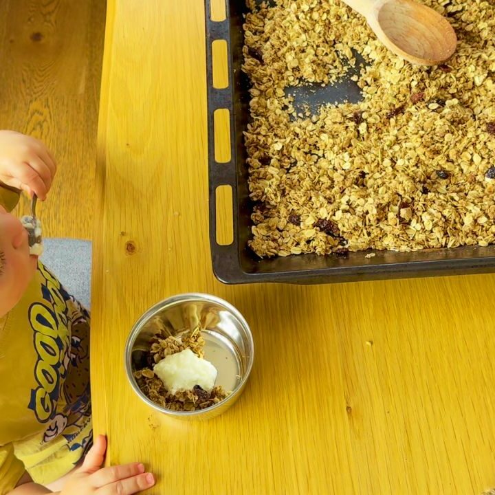 Toddler serving himself homemade granola with yoghurt at the table, part of our simple gut-friendly breakfast rhythm.