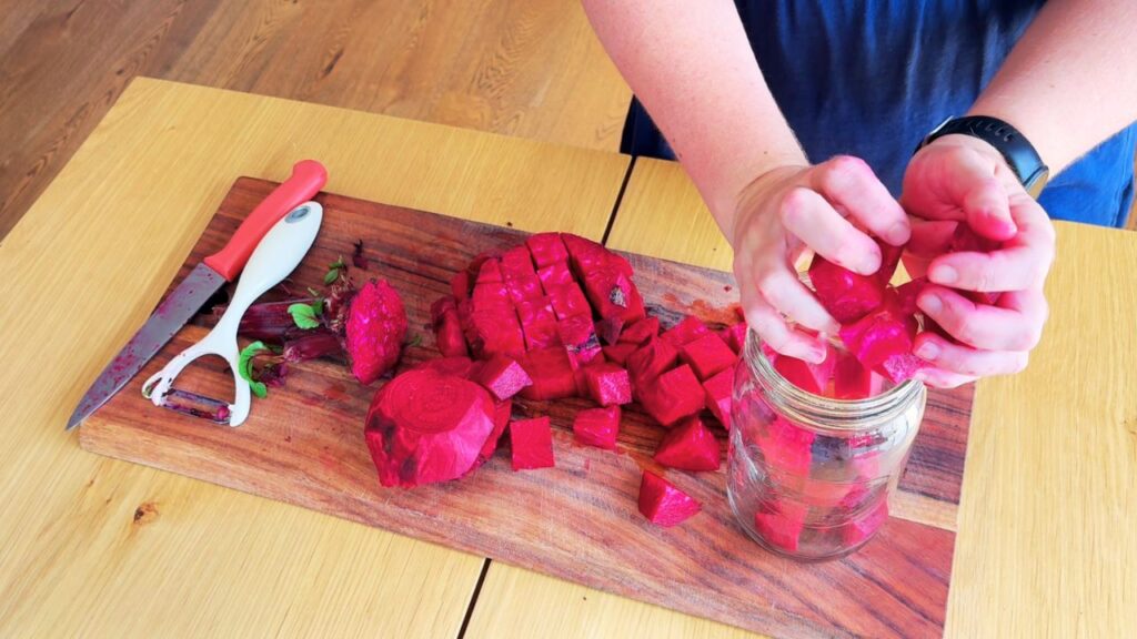 Adding chopped beetroot into a glass jar for homemade beetroot kvass