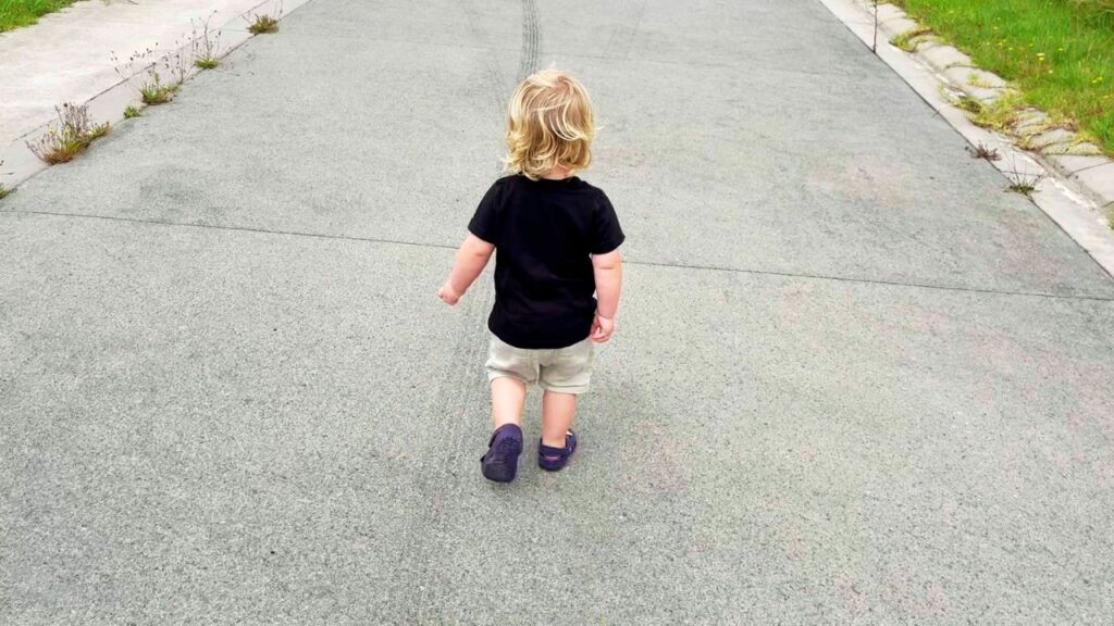 Toddler walking independently down a quiet road, exploring at their own pace.