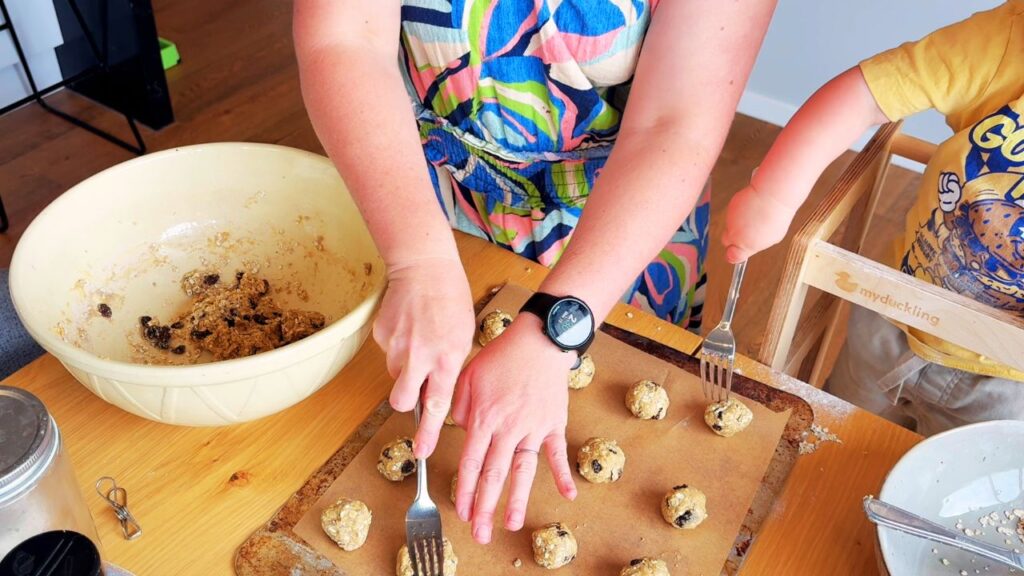 Making toddler oat and raisin cookies together, gently flattening cookie dough before baking
