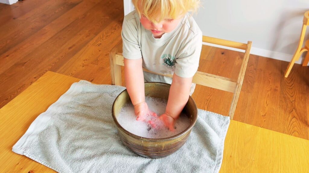 Toddler washing hands independently in a bowl as part of a gentle morning routine
