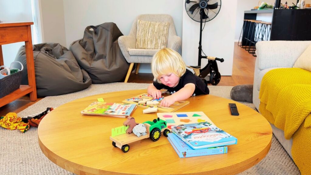 Toddler playing quietly with books and wooden toys in a calm, home-centred environment.